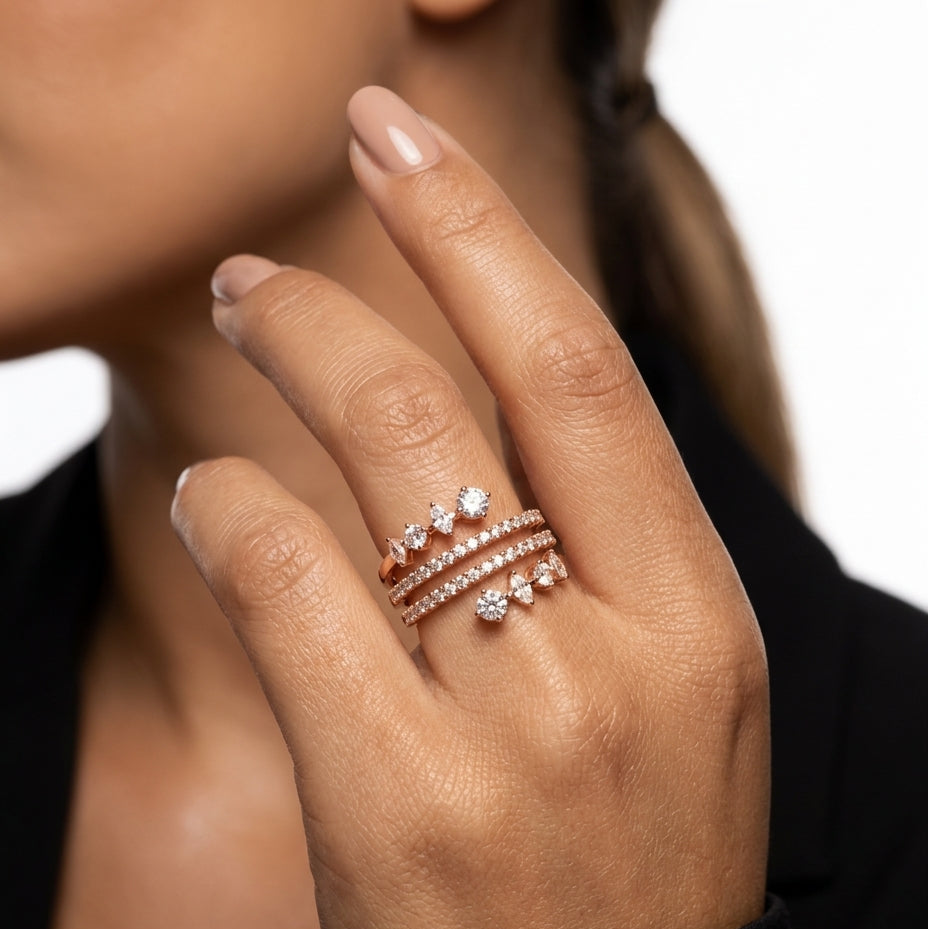 Hand wearing multiple diamond rings on a neutral background